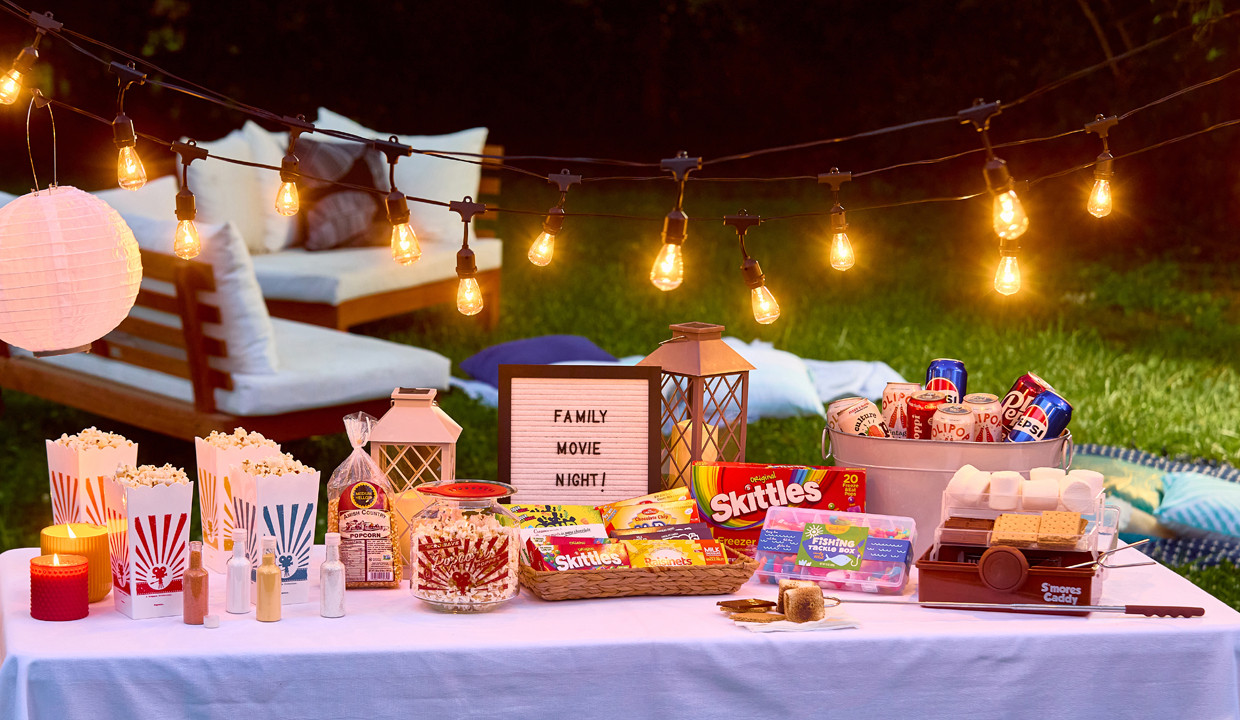 Snack table at an outdoor movie night with popcorns kit, s'mores kit, candy tackle box, theater boxed candy, and more.
