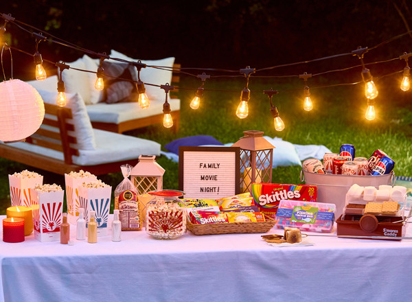 Snack table at an outdoor movie night with popcorns kit, s'mores kit, candy tackle box, theater boxed candy, and more.