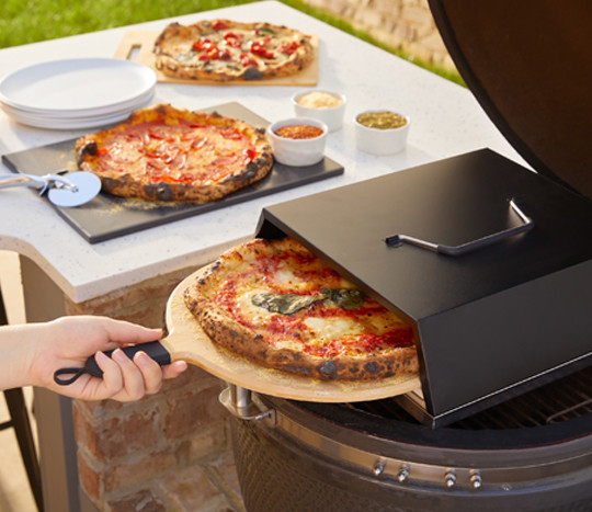 Woman making pizza with a grill-top pizza oven, pizza stone, and accessories.