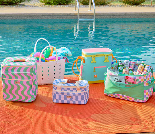 Cooler and bags filled with drinks and toys next to pool.