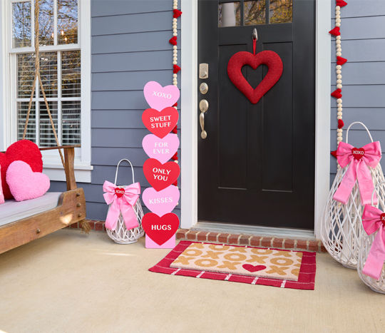 Front porch decorated with white woven lanterns, and heart-themed wreath, pillows, coir mat, garland & more.