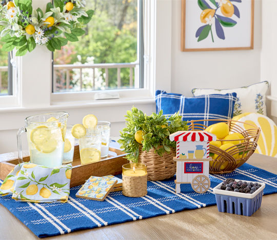 Breakfast nook with lemon-themed decor: wall art, lemon wreath, pillows, wooden crate, rattan basket & more.