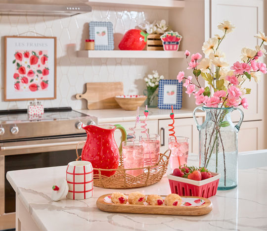 Strawberry-themed kitchen accessories and decor: strawberry pitcher and cookie jar, wall art, wooden tray & bowl, candles, vase & more.