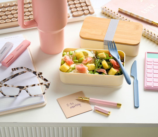 Work desk with bento box food storage container, blue-light blocking glasses, 40-oz. water bottle, and desk supplies.