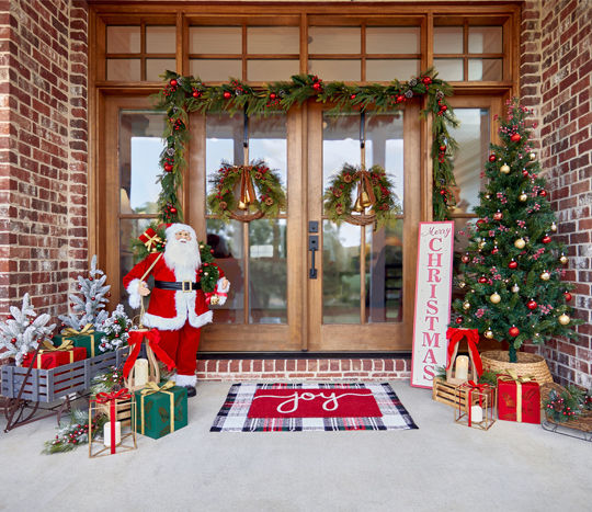 Front porch decorated for Christmas with 6-ft lighted trees, 3-ft. potted trees with fairy lights, sled porch leaner, wooden trees, garland & wreaths, and gold lanterns.