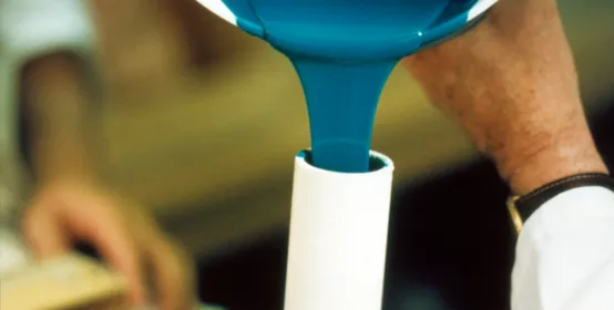 Man's hands pour mixed Silastic moldmaking rubber into a tube.