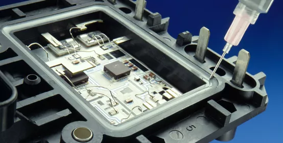 Thermal Cure Adhesive is applied to an automotive control module assembly with a syringe. 1988 NEPCON Show materials