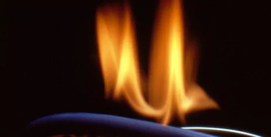 Image (probably shot for Materials News in the early 1980s) of beaker containing clear fluid, various molded rubber items and a fluorosilicone O-ring, with flame to symbolize heat- and flame-resistance. High-temperature performance.