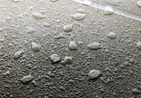 Water drops beading on concrete surface treated with AllGuard Concrete Sealer water repellent treatment. Seam with sealant in joint in upper right corner.