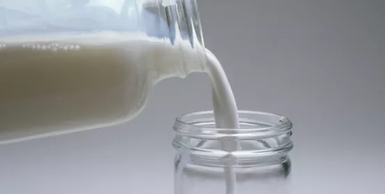 Pouring milky emulsion from a bottle into a jar. Materials News / product promotion