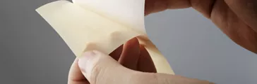 Hands pulling a sticker off of release backing paper