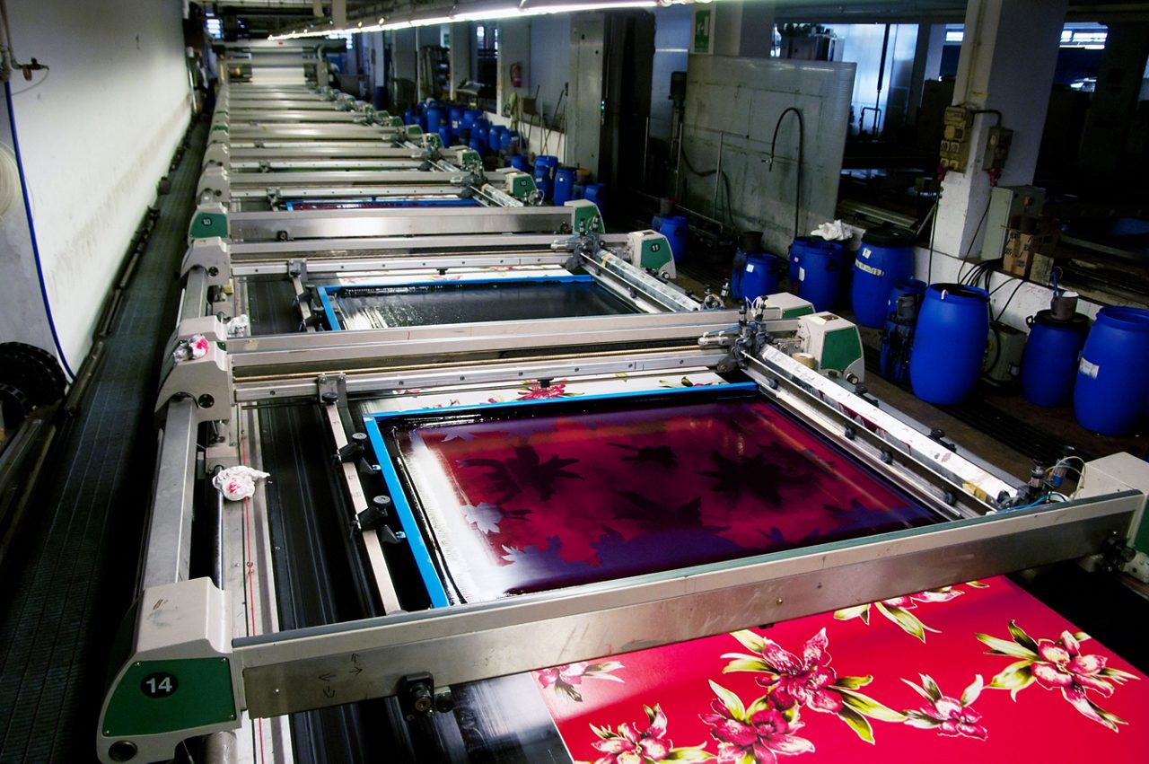 Textile printing in a factory. Textile printing is the process of applying color to fabric in definite patterns or designs. In properly printed fabrics the color is bonded with the fiber, so as to resist washing and friction. / Dreamstime Image #23920899