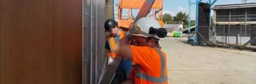Worker in orange vest/shirt installing cladding panel