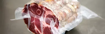 Roll of air cured pork covered in wrapping on metal table in food processing plant