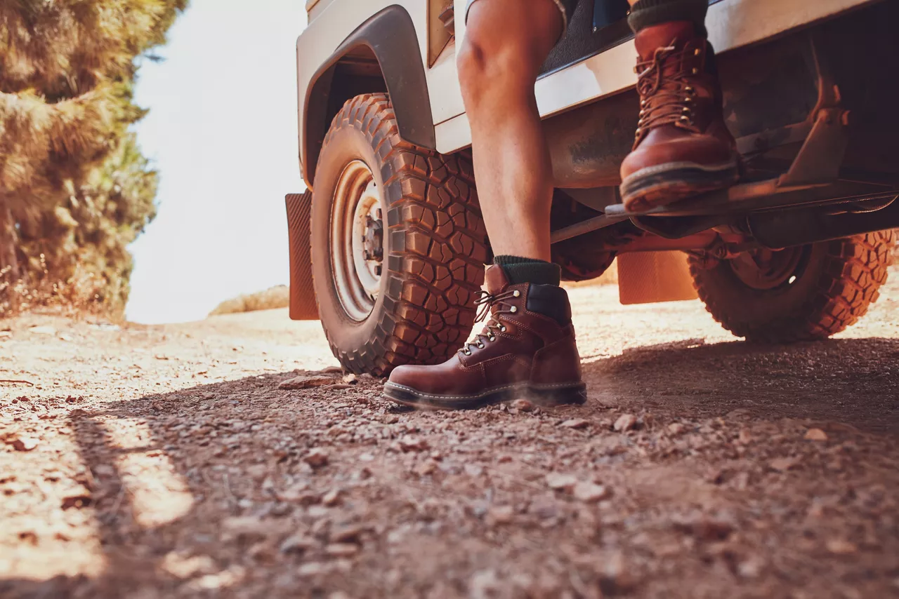 Close-up of male leg with leather boot stepping out of a off road vehicle. Car parked on the dirt road in countryside.