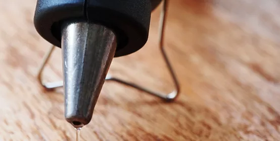 Closeup hot glue gun with melted glue dripping out.