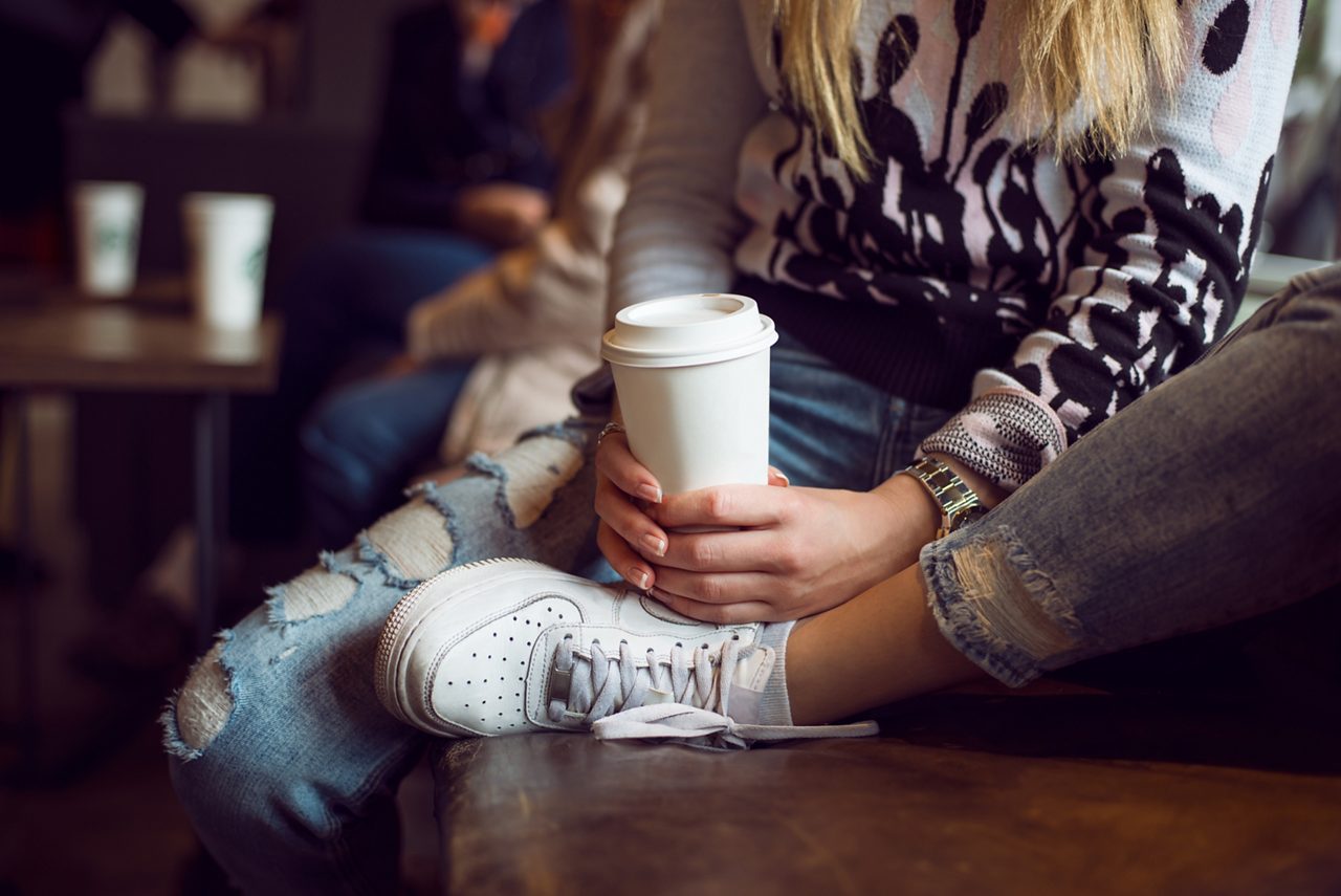 Woman hands holding paper coffee cup while sitting in coffee shop