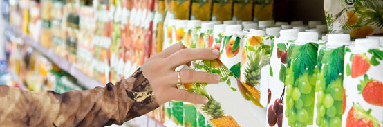 Close up of female hand grabbing paper carton of pineapple juice from grocery store shelf