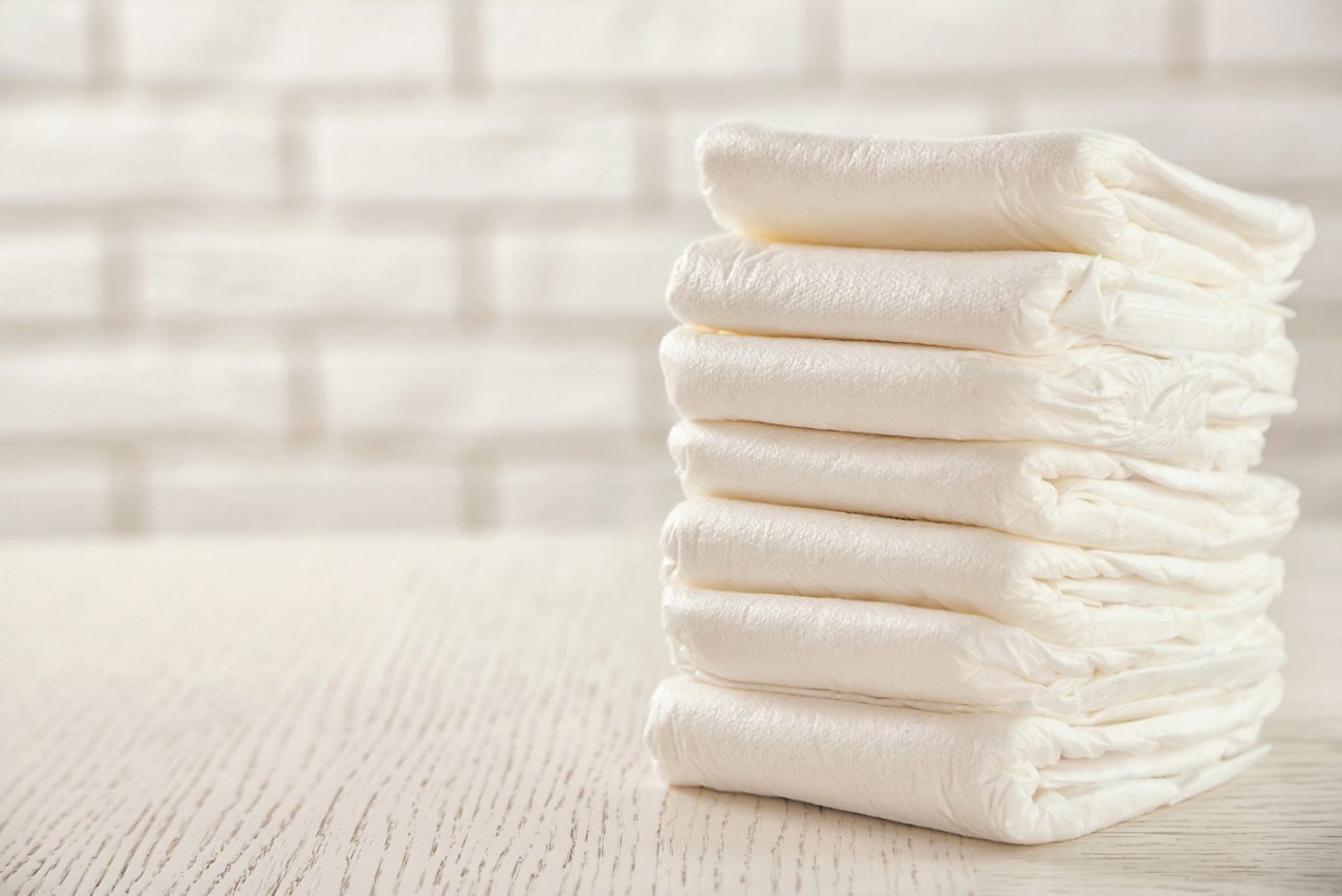 Stack of white diapers on white wood table with white brick wall in background