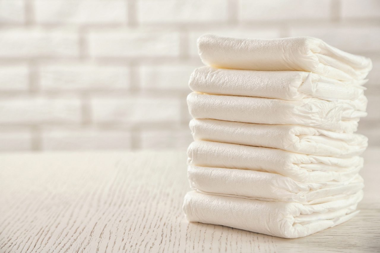 Stack of white diapers on white wood table with white brick wall in background