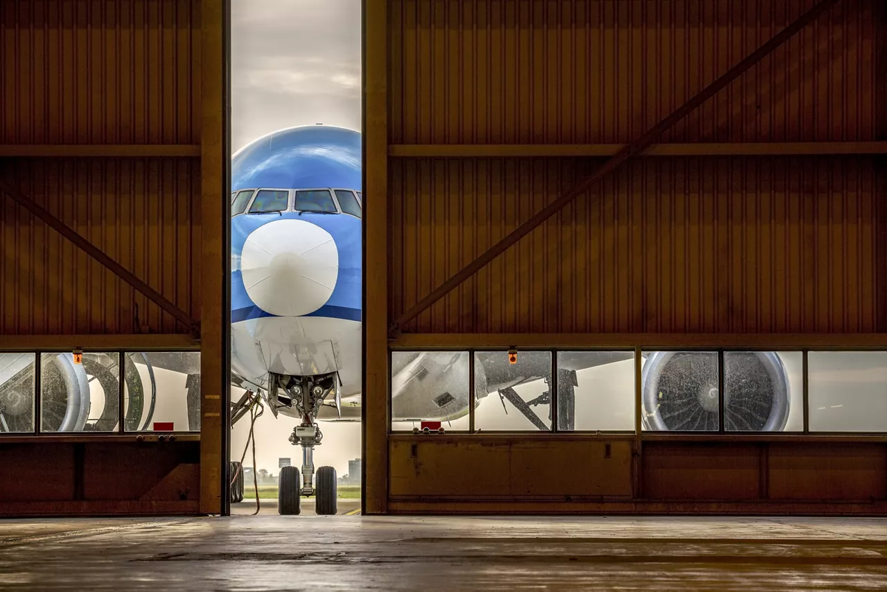 Blue airplane in front of half opened door to hangar.