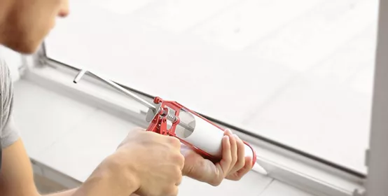 Man squeezing caulk onto window seal