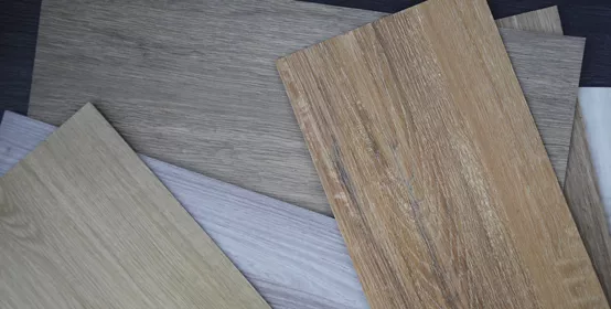 Samples of laminate and vinyl floor tile on wooden background.