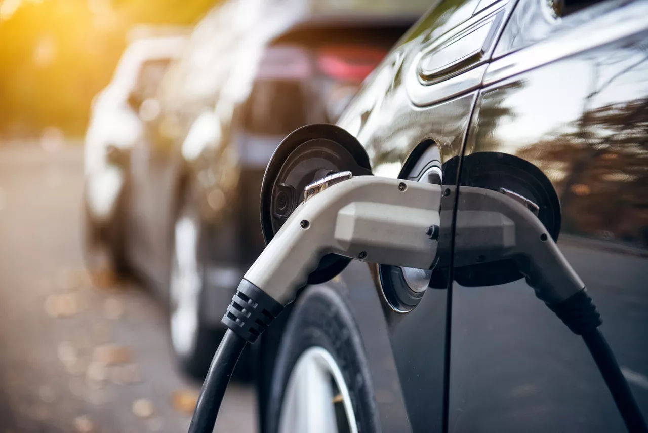 Electric car charging on parking lot with electric car charging station on city street. Electric cars in the row ready for charge. Close up of power supply plugged into electric car being charged