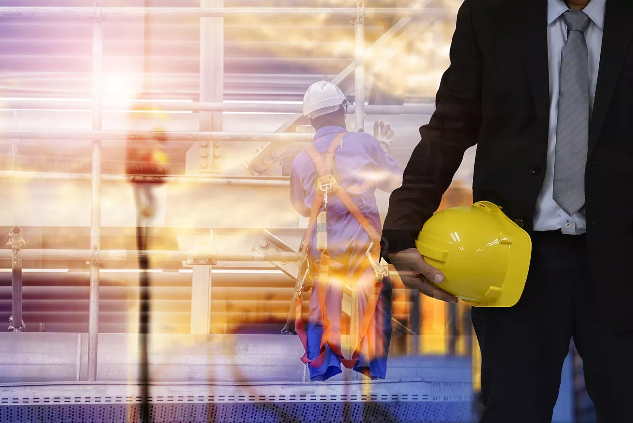 Construction safety concept, engineer holding yellow hardhat and blurred construction background.