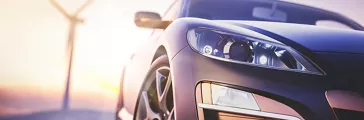 Sports car parked in front of a wind turbine at sunrise or sunset.