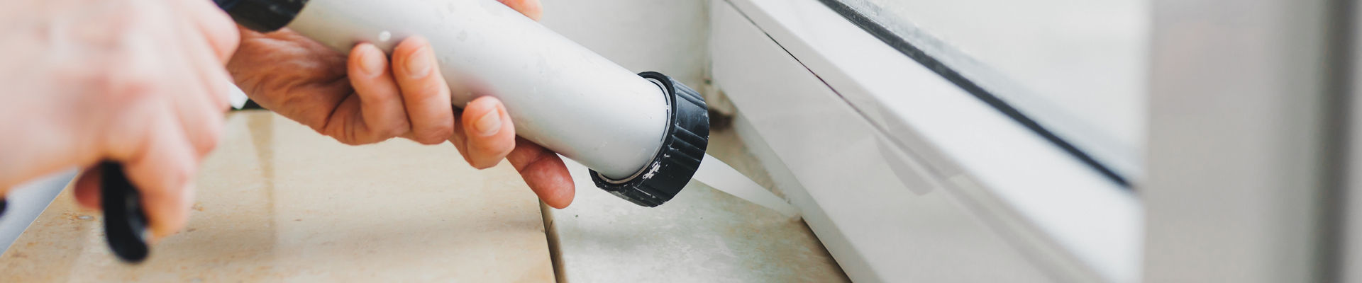 Worker applies silicone sealant to window 