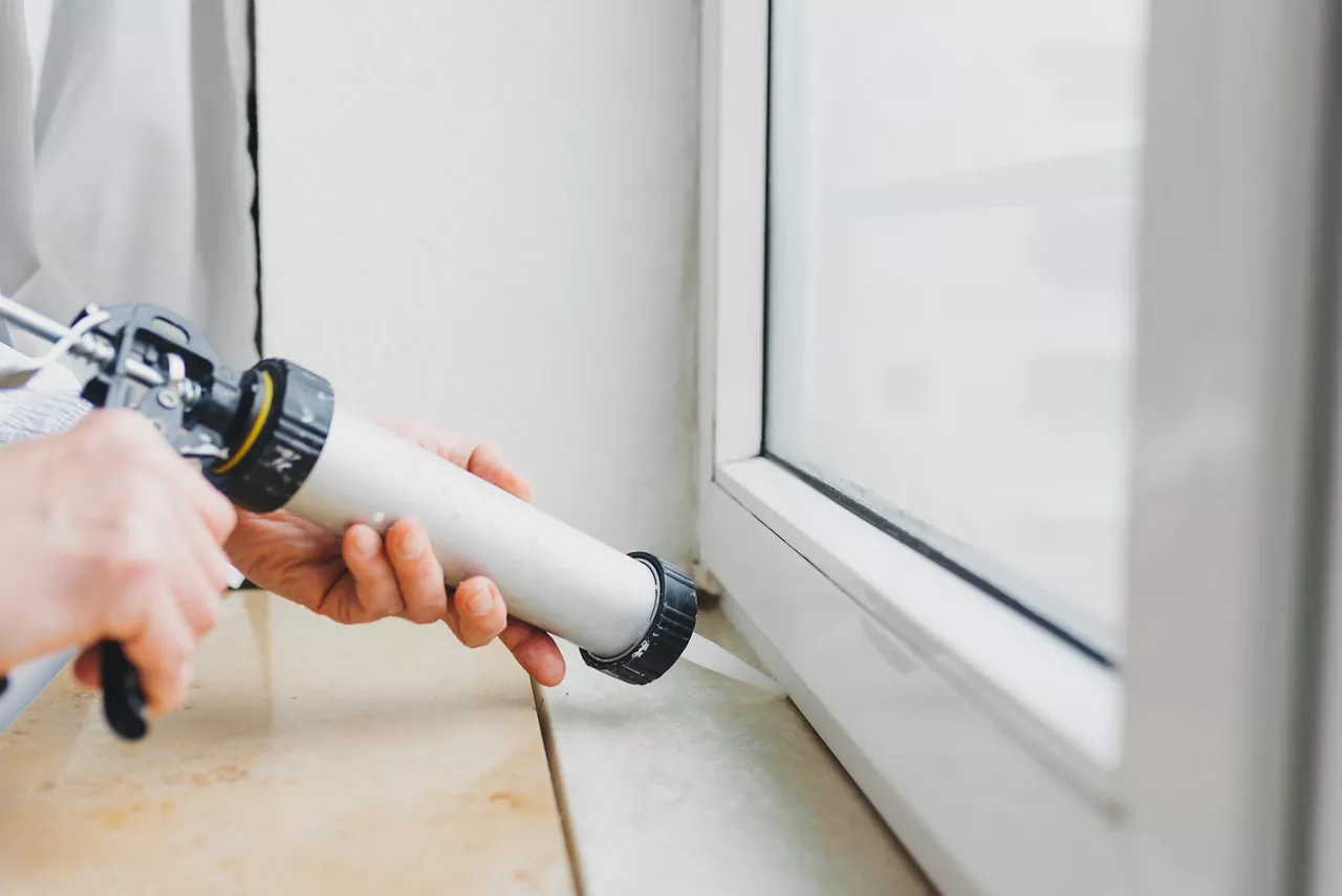 Hands of worker using a silicone tube to repair a window indoors.