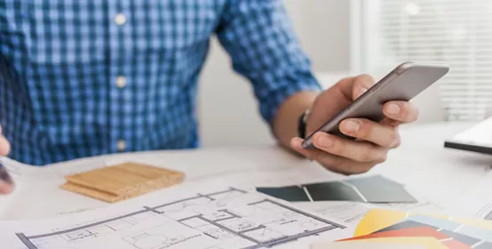 Man reviewing blueprint with phone in hand