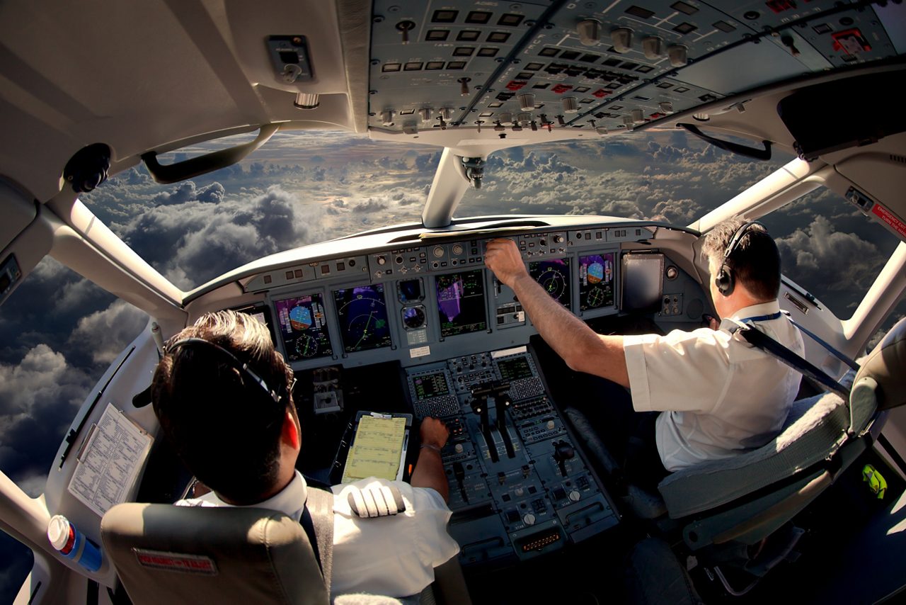 Two pilots on flight deck of modern passenger jet aircraft looking out over clouds.