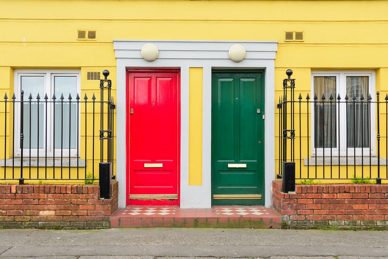 Yellow building with red and green doors.  Surrounded by a metal fence.