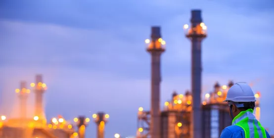 Worker with clipboard looking at oil refinery plant at sunrise