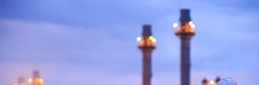 Worker with clipboard looking at oil refinery plant at sunrise.