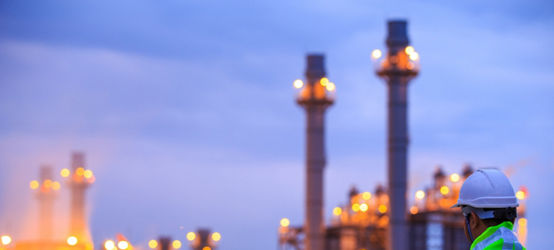 Worker with clipboard looking at oil refinery plant at sunrise.