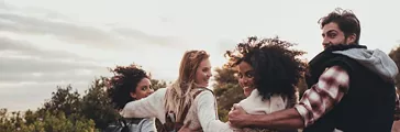 Friends hiking in nature. Group of man and women walking together in countryside. Happy young people turning around and looking at camera.