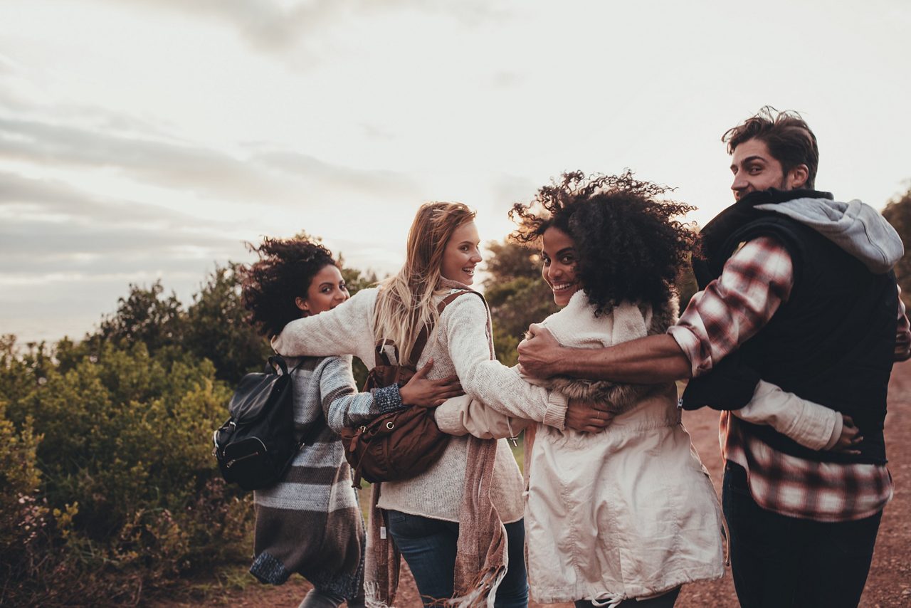 Friends hiking in nature. Group of man and women walking together in countryside. Happy young people turning around and looking at camera.