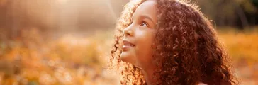 Afro american happiness little girl with curly hair receives miracle sun rays from the sky