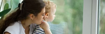 Young mother and son watching the rain through the window
