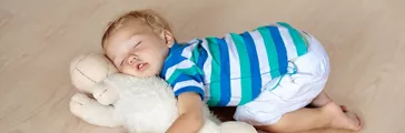  Baby sleeping on wooden floor with stuffed toy sheep and milk bottle