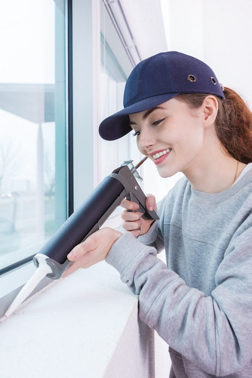 Young woman using caulking gun on window frame