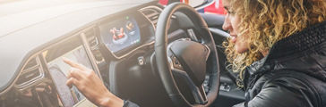 Young woman sits behind wheel in car and uses an electronic dashboard, tablet computer. Girl is traveler looking for a way through navigation system. Trip, caravanning, tourism, journey.