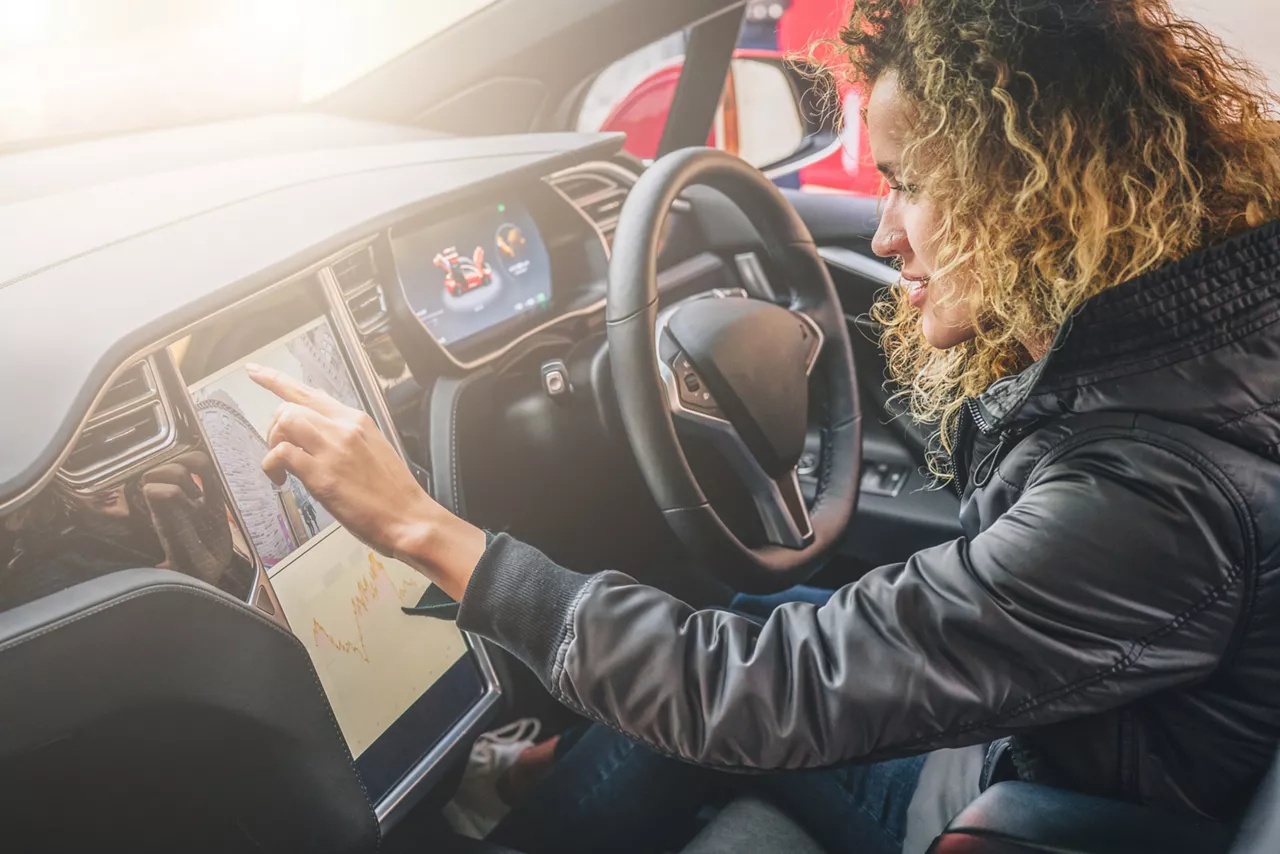 Woman sits behind wheel in car and uses electronic dashboard