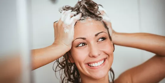 Beautiful smiling young woman washing her long hair with shampoo.