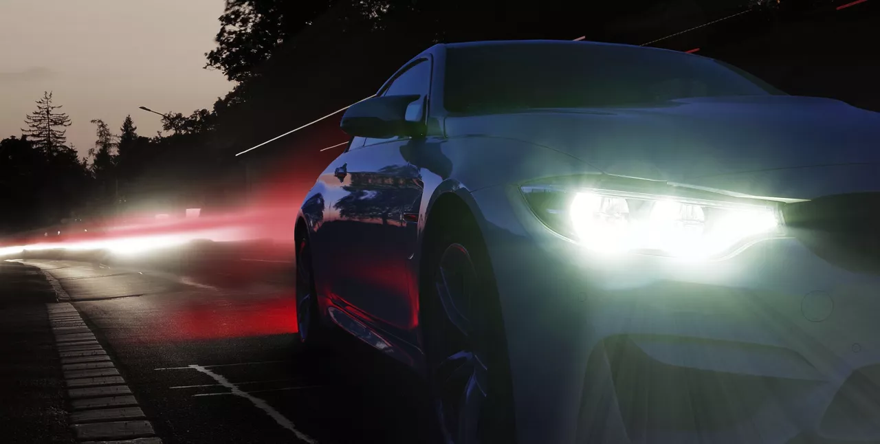 Headlights of a sports car at night with other lights in the background.