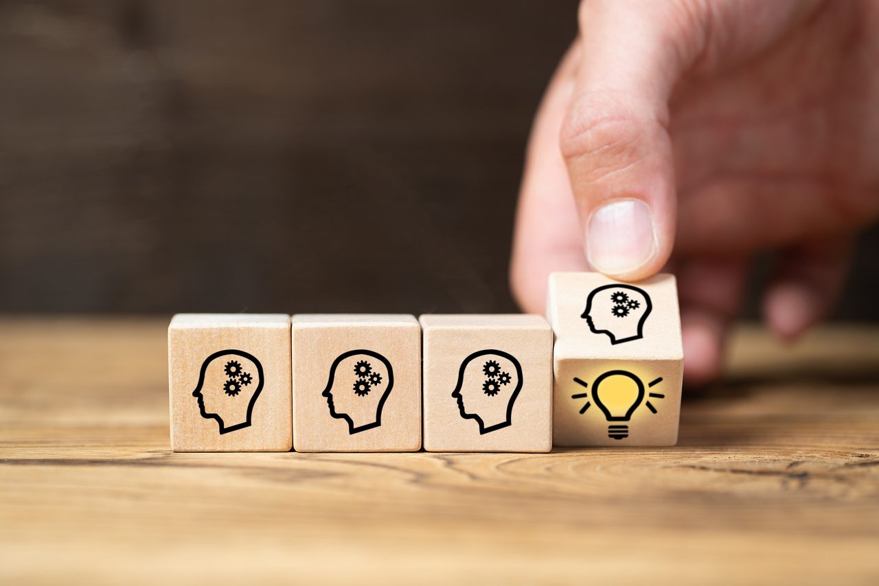 Hand lining up wooden blocks with a human head outline with gears and a lightbulb icon on bottom of the last block.