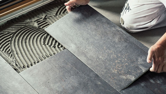 Worker placing a ceramic floor tile on an adhesive surface